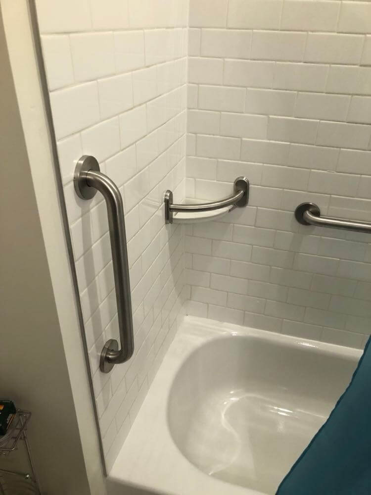 A bathtub and shower wall with handrails