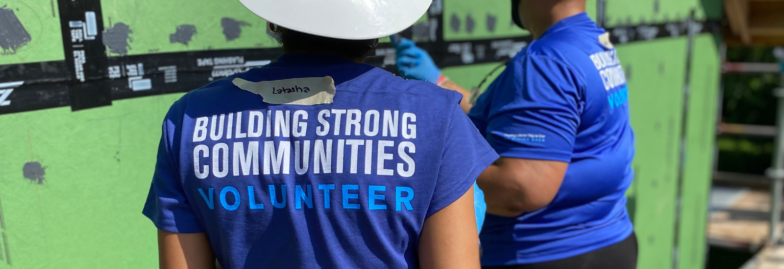 Two people wearing blue t-shirts that read "Building Strong Communities Volunteer" on the back