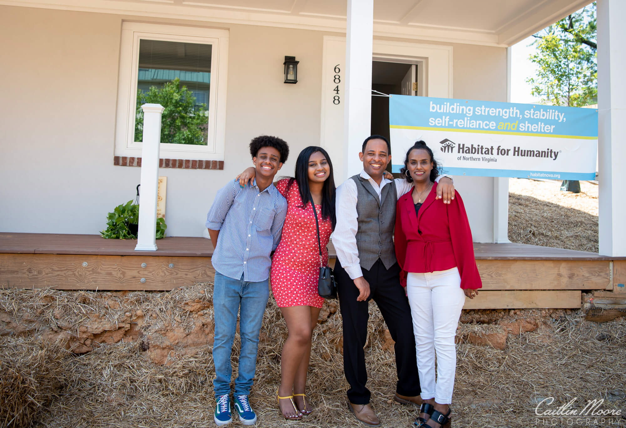 family of four smiling in front of their new home