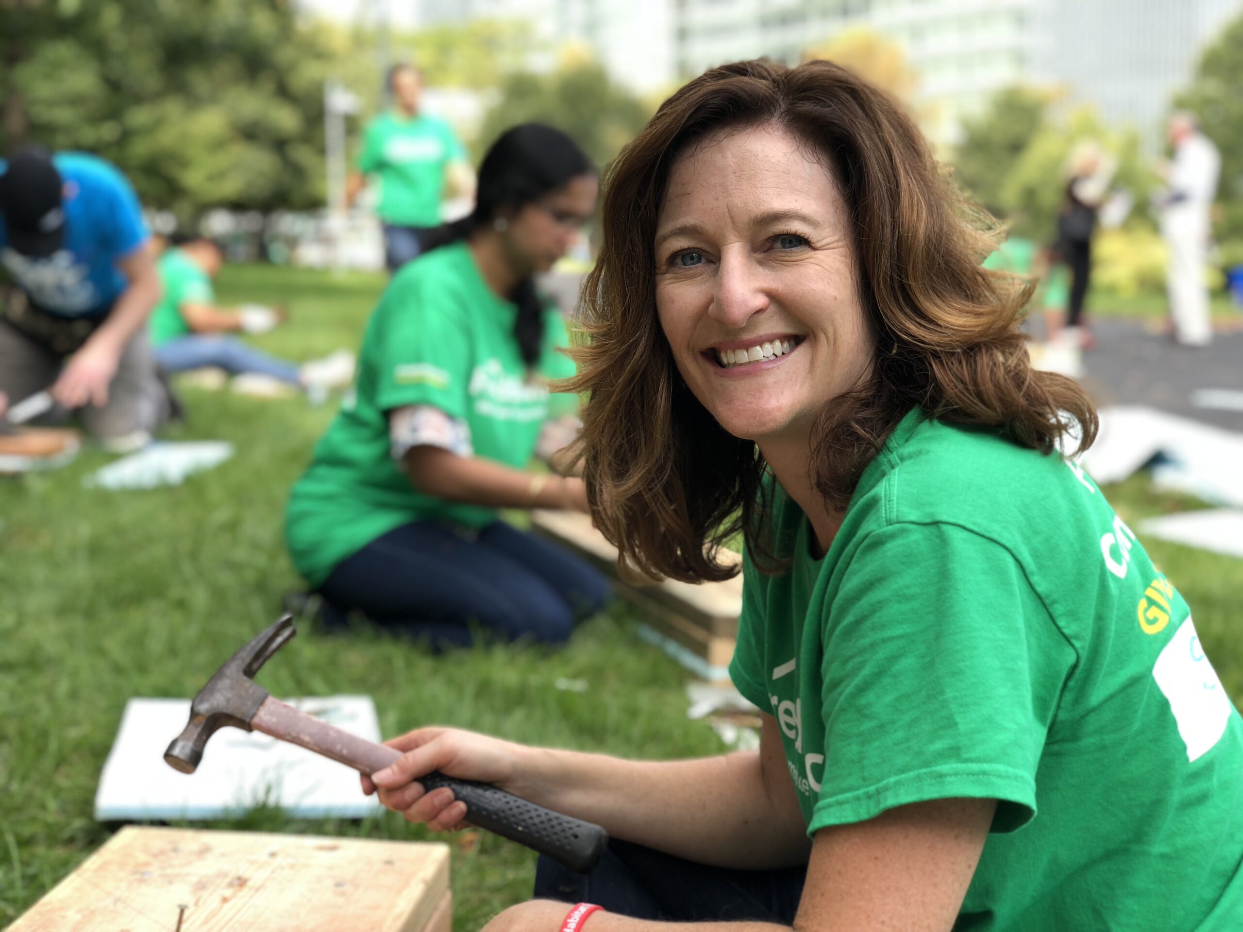 woman in green shirt smiling at camera holding a hammer
