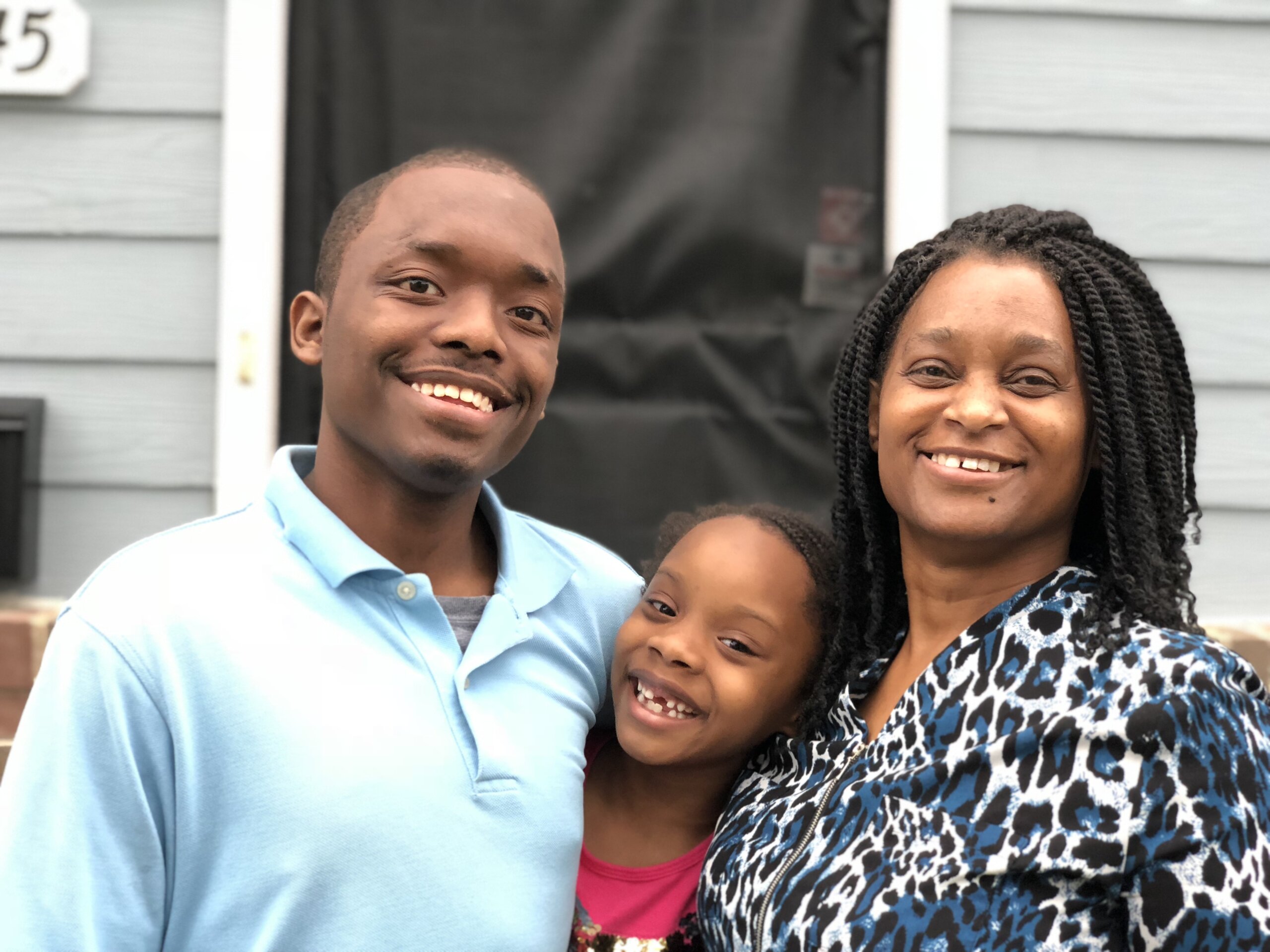 family of three smiling in front of home